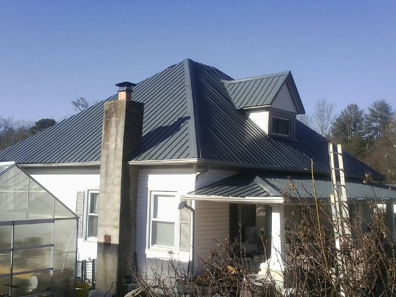 Dark blue standing seam metal roof on a white farmhouse with dormer — Slate & Tile Roof Repair by Roofing Brothers in Winfred