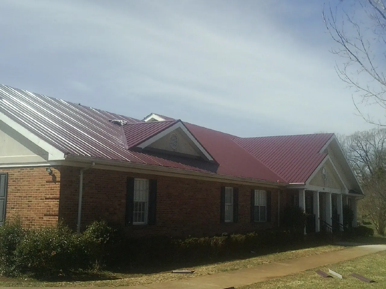 Red metal roof with gabled entries on a long brick building, from a Hail Damage Roof Repair job in Winfred