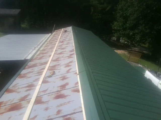 Old rusted panels beside newly installed green metal roofing — Wind Damage Roof Repair by Roofing Brothers in Winfred