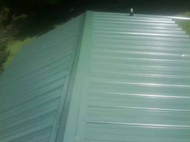 New green metal panels meeting at the ridge of a roof — Flat Roof Repair work by our crew in Winfred
