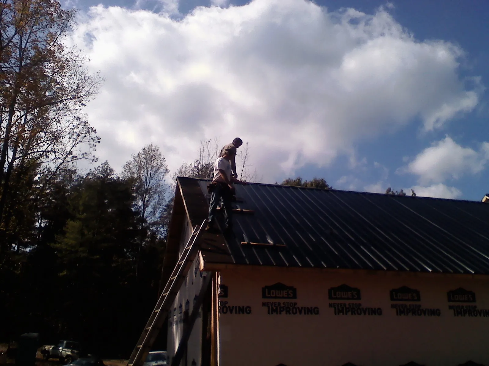 Roofer fastening dark metal panels high against a cloudy sky, from a Roof Inspection job in Winfred